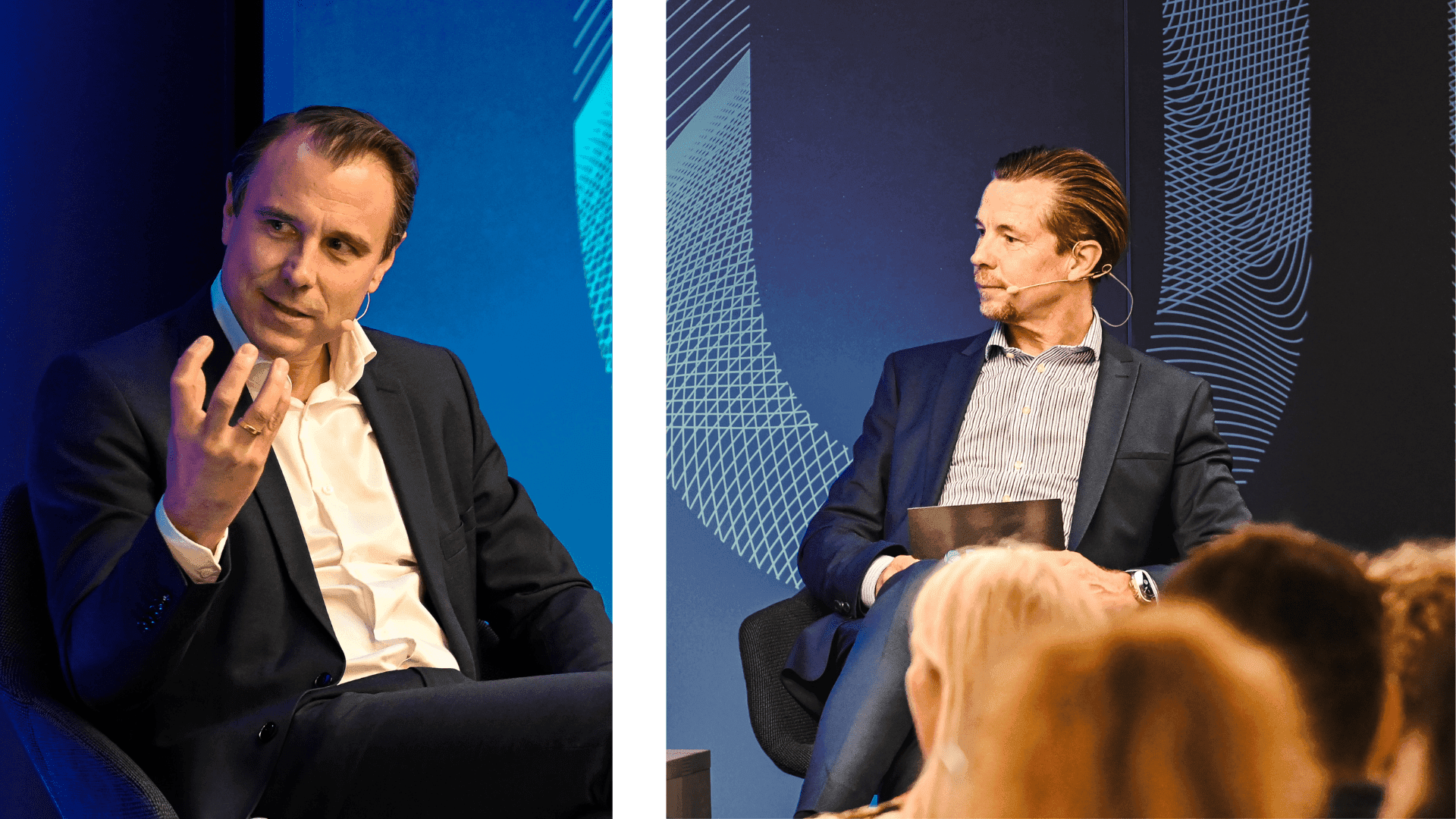 Two men in suits engaged in a discussion on stage, with one speaking animatedly and the other listening attentively. Audience visible in foreground.