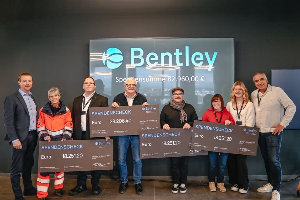 A group of people holding large donation checks in front of a sign that reads "Bentley" with a total donation amount displayed above.