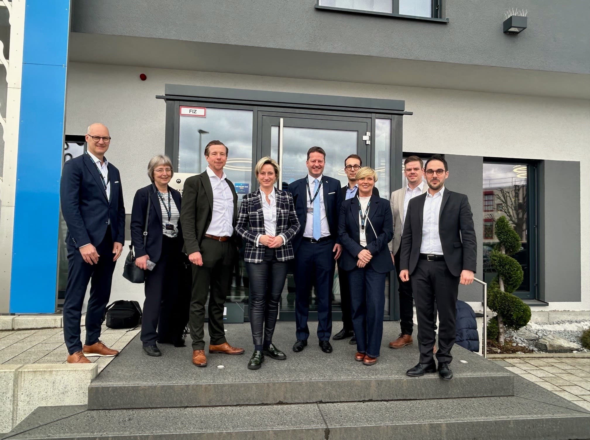 A group of nine people in business attire stand on steps outside a building, smiling at the camera.
