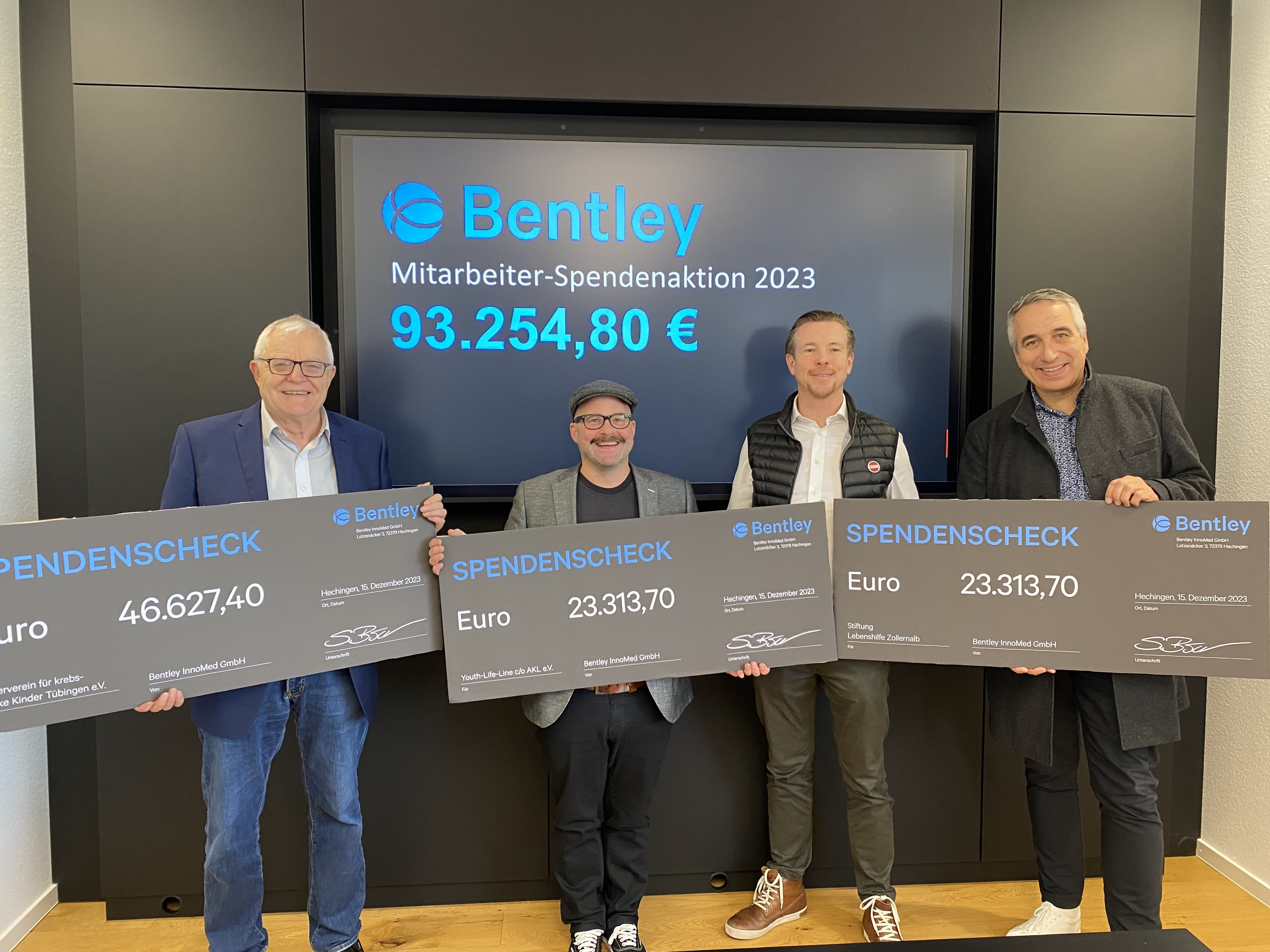 Four men holding large donation checks in front of a screen displaying "Bentley Mitarbeiter-Spendenaktion 2023" and a total amount of 93,254.80 €.