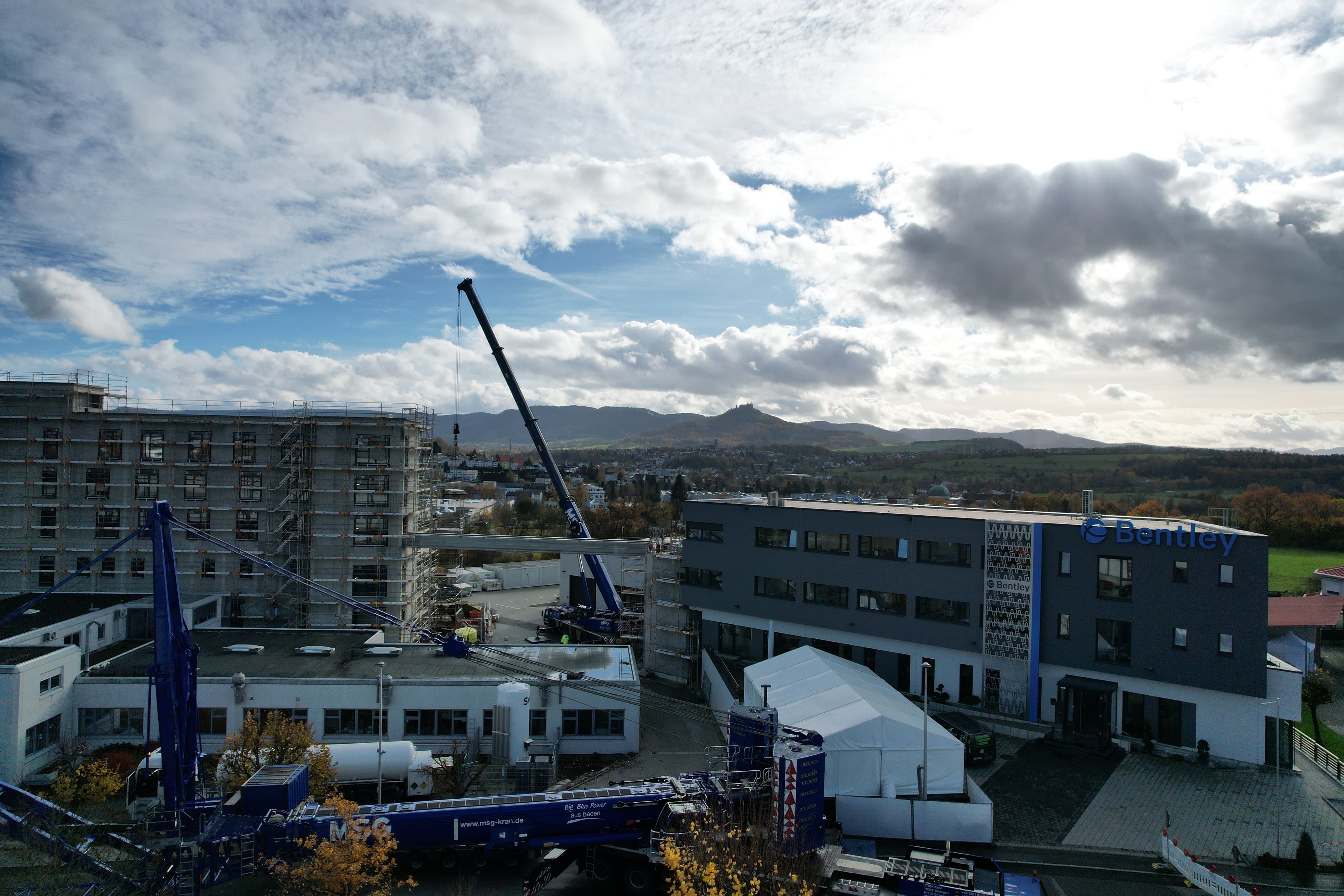Construction site with cranes, buildings, and a distant mountain under a partly cloudy sky.